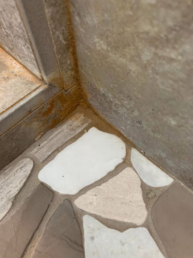 Stone shower corner with buildup before cleaning